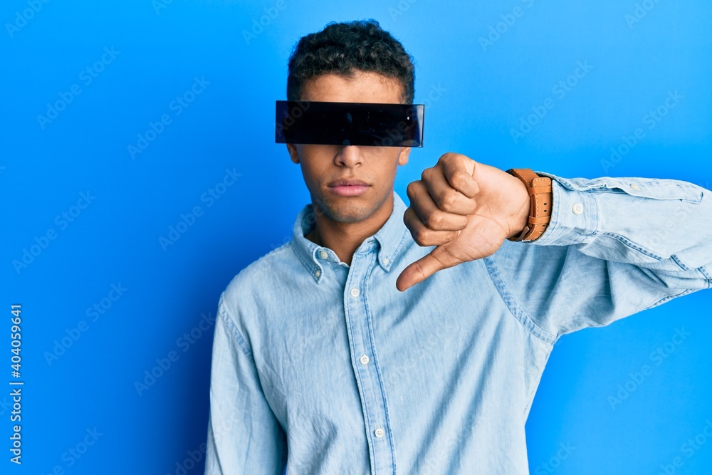 Fototapeta premium Young handsome african american man wearing banner glasses covering eyes with angry face, negative sign showing dislike with thumbs down, rejection concept