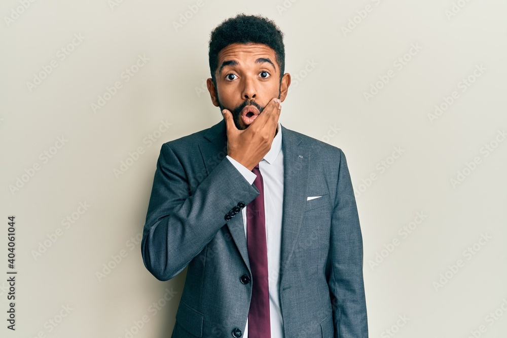 Handsome hispanic man with beard wearing business suit and tie looking fascinated with disbelief, surprise and amazed expression with hands on chin Handsome hispanic man with beard wearing business suit and tie looking fascinated with disbelief, surprise and amazed expression with hands on chin