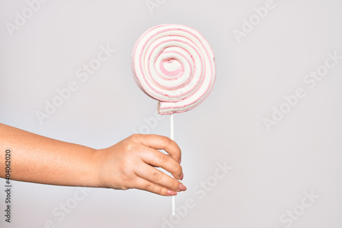 Hand of caucasian young woman holding sweet pink lollipop over isolated white background