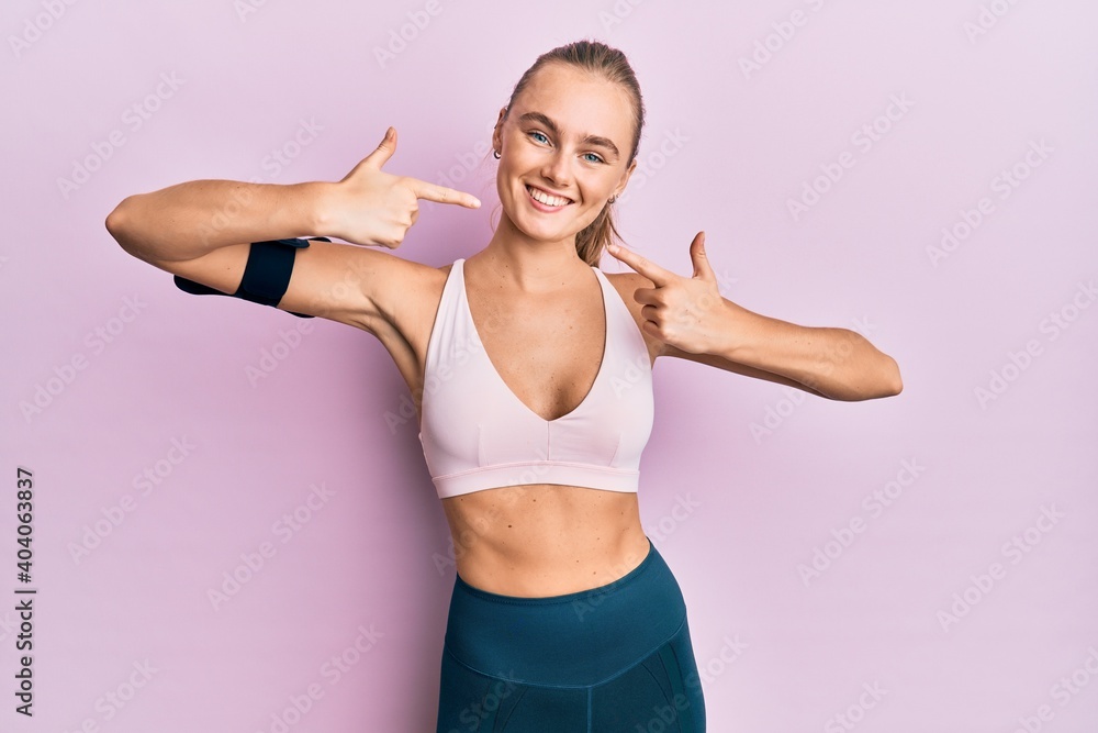 Beautiful blonde woman wearing sportswear and arm band smiling cheerful showing and pointing with fingers teeth and mouth. dental health concept.