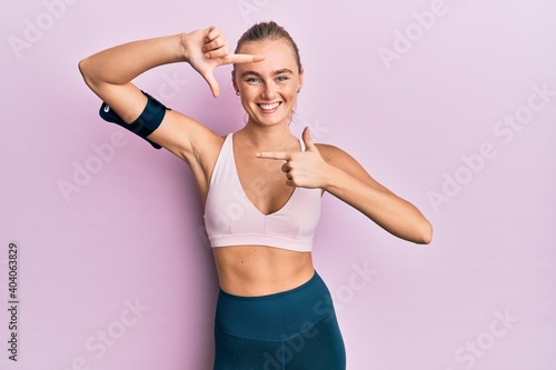 Beautiful blonde woman wearing sportswear and arm band smiling making frame with hands and fingers with happy face. creativity and photography concept.