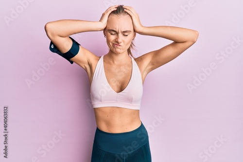 Beautiful blonde woman wearing sportswear and arm band suffering from headache desperate and stressed because pain and migraine. hands on head. © Krakenimages.com