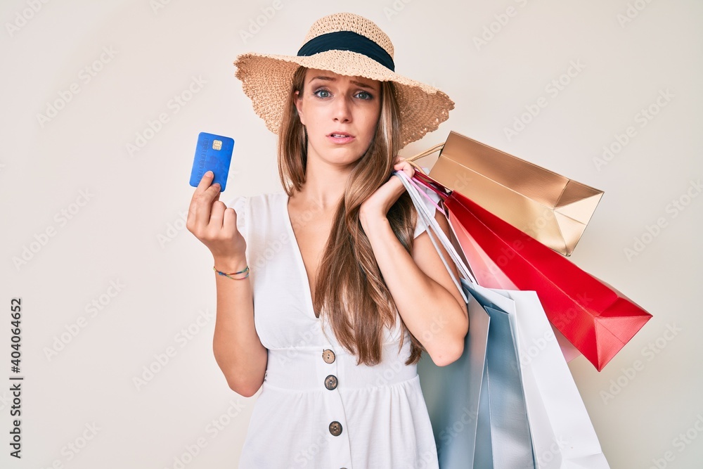 Young blonde girl holding shopping bags and credit card clueless and confused expression. doubt concept. Young blonde girl holding shopping bags and credit card clueless and confused expression. doubt concept.