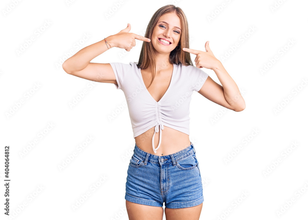 Young beautiful blonde woman wearing casual white tshirt smiling cheerful showing and pointing with fingers teeth and mouth. dental health concept. Young beautiful blonde woman wearing casual white tshirt smiling cheerful showing and pointing with fingers teeth and mouth. dental health concept.