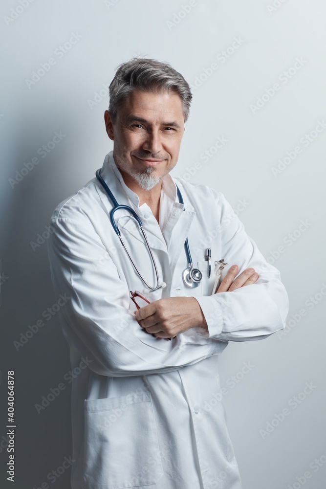 Portrait of trustworthy older confident doctor with gray hair wearing white lab coat standing against wall, smiling. Portrait of trustworthy older confident doctor with gray hair wearing white lab coat standing against wall, smiling.