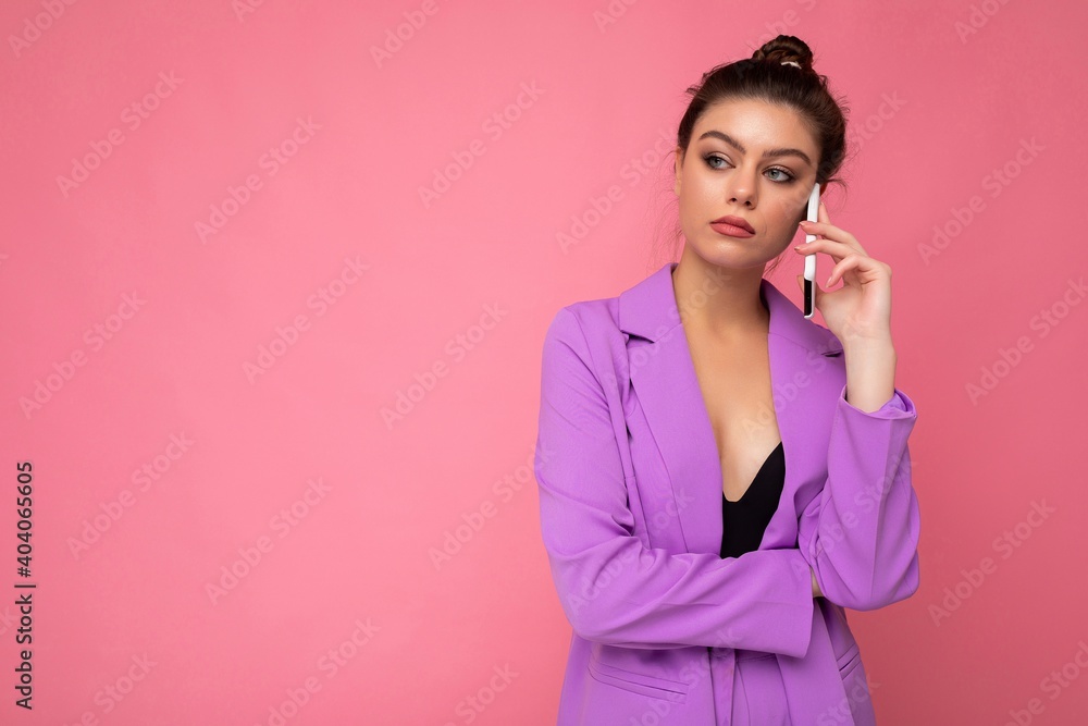 dissatisfied beautiful young woman wearing purple suit talking on the mobile phone isolated over pink background looking to the side dissatisfied beautiful young woman wearing purple suit talking on the mobile phone isolated over pink background looking to the side