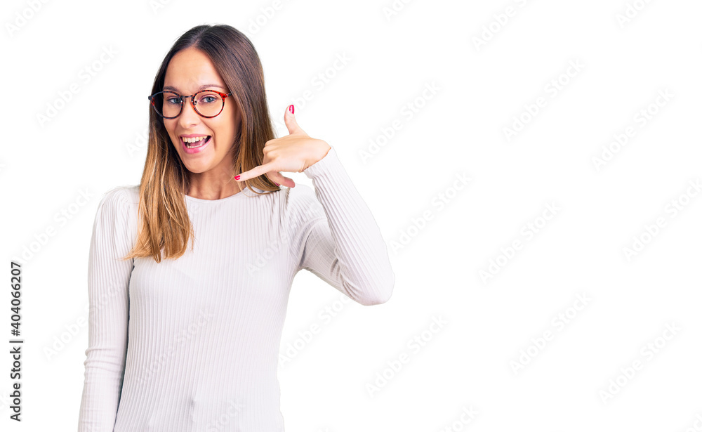 Beautiful brunette young woman wearing casual white sweater and glasses smiling doing phone gesture with hand and fingers like talking on the telephone. communicating concepts. Beautiful brunette young woman wearing casual white sweater and glasses smiling doing phone gesture with hand and fingers like talking on the telephone. communicating concepts.