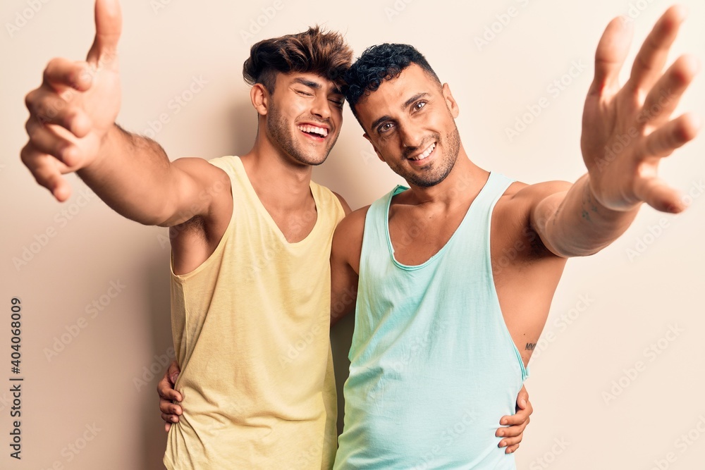 Young gay couple wearing casual clothes looking at the camera smiling with open arms for hug. cheerful expression embracing happiness. Young gay couple wearing casual clothes looking at the camera smiling with open arms for hug. cheerful expression embracing happiness.