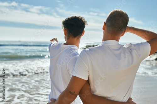 Young gay couple on back view looking to the horizon at the beach.