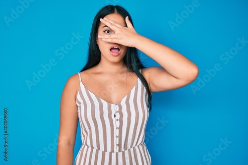 Young beautiful asian girl wearing casual clothes peeking in shock covering face and eyes with hand, looking through fingers with embarrassed expression.