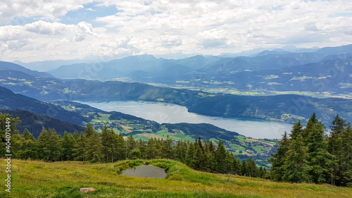 A panoramic view on the Millstaettersee lake from Granattor in Austrian Alps. The distant lake is surrounded by high mountains. Few clouds above. Endless mountain chains. Lush and vast pasture. Relax