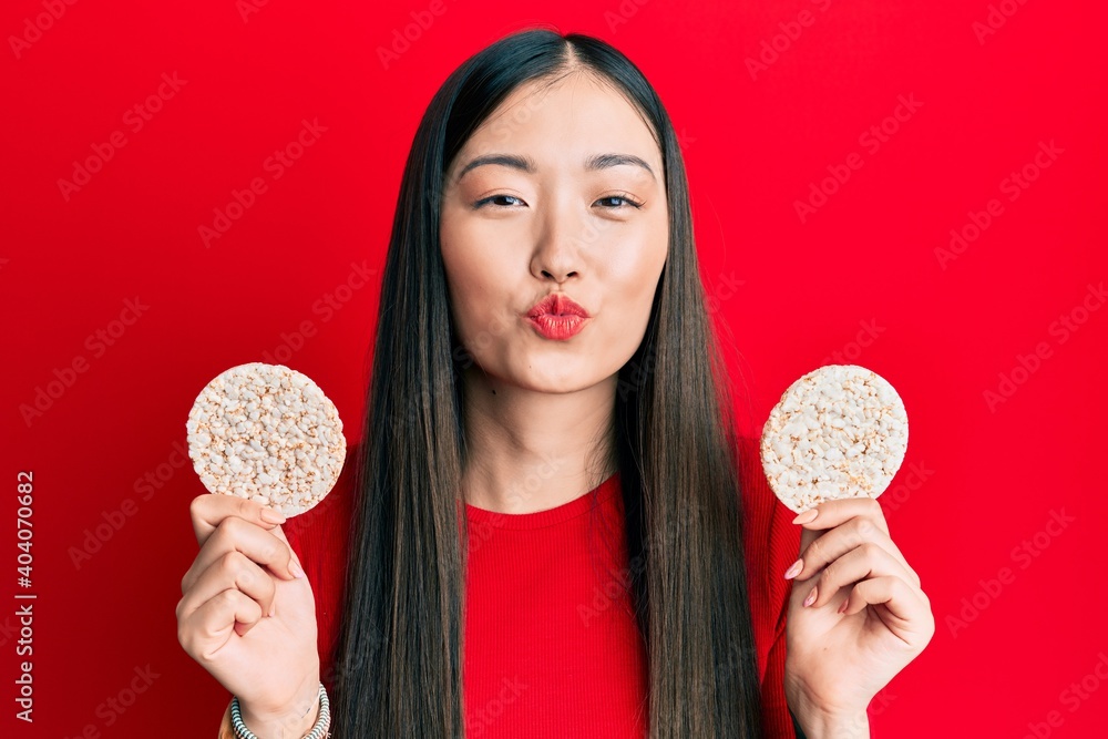 Young chinese woman eating healthy rice crackers looking at the camera blowing a kiss being lovely and sexy. love expression. Young chinese woman eating healthy rice crackers looking at the camera blowing a kiss being lovely and sexy. love expression.