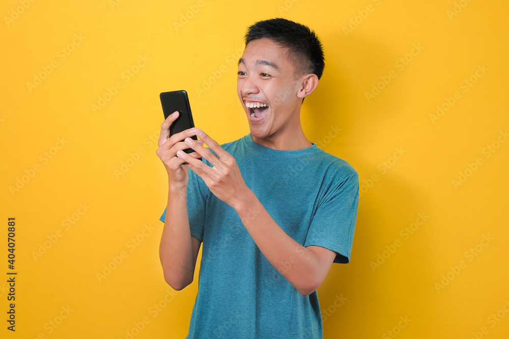 Shocked face of Asian man in casual blue t-shirt looking at phone screen Shocked face of Asian man in casual blue t-shirt looking at phone screen