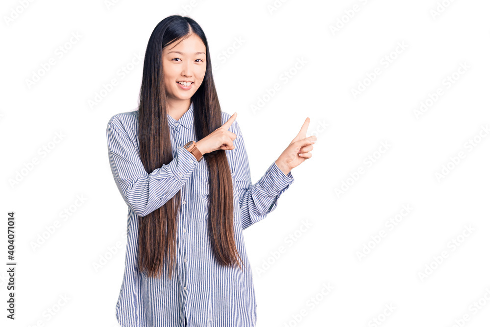 Young beautiful chinese woman wearing casual shirt smiling and looking at the camera pointing with two hands and fingers to the side. Young beautiful chinese woman wearing casual shirt smiling and looking at the camera pointing with two hands and fingers to the side.