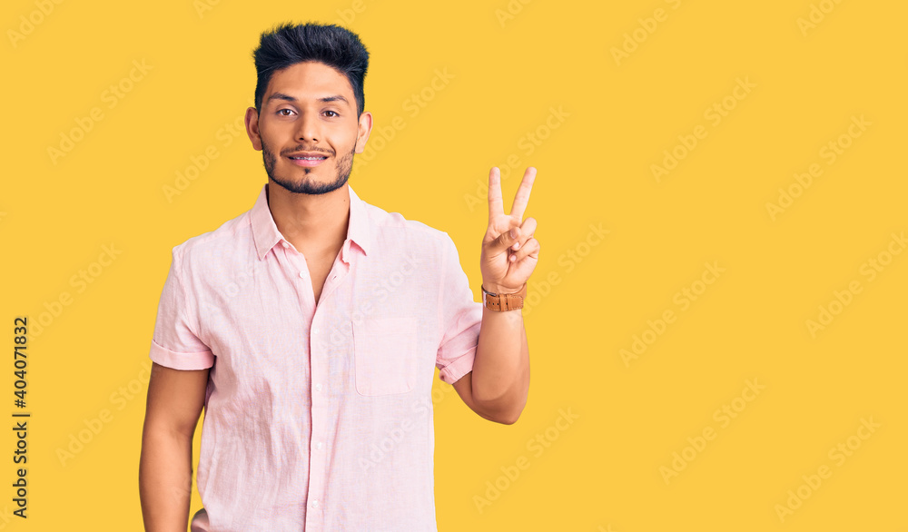 Handsome latin american young man wearing casual summer shirt smiling looking to the camera showing fingers doing victory sign. number two. Handsome latin american young man wearing casual summer shirt smiling looking to the camera showing fingers doing victory sign. number two.