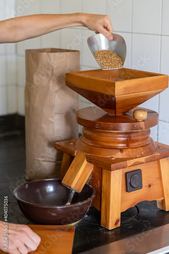 Getreidemühle aus Holz wird mit Gerste befüllt, dahinter steht der Sack der befüllt werden wir dmit dem Mehl