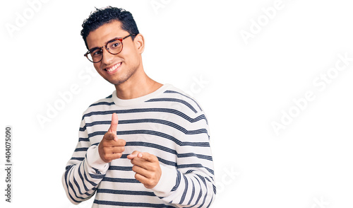 Hispanic handsome young man wearing casual clothes and glasses pointing fingers to camera with happy and funny face. good energy and vibes.