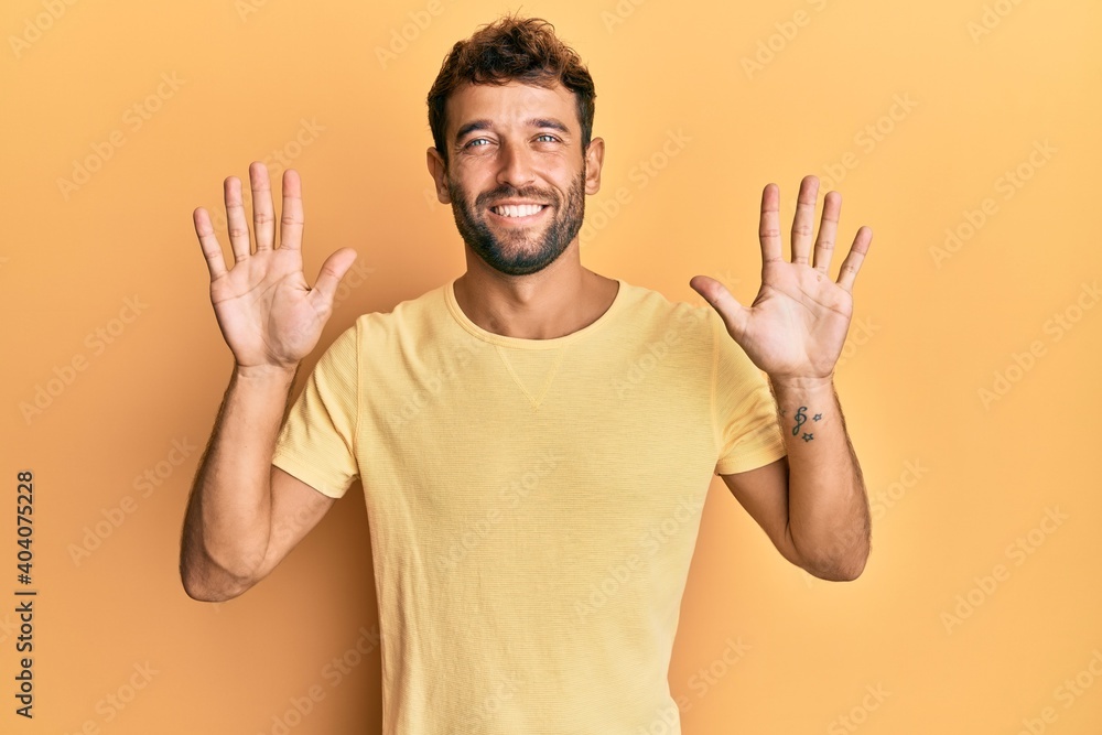 Handsome man with beard wearing casual yellow tshirt over yellow background showing and pointing up with fingers number ten while smiling confident and happy. Handsome man with beard wearing casual yellow tshirt over yellow background showing and pointing up with fingers number ten while smiling confident and happy.