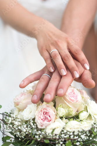 Brautpaar hält Hände mit Eheringen über den Brautstrauß aus weißen Rosen