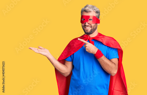 Young blond man wearing super hero custome amazed and smiling to the camera while presenting with hand and pointing with finger. photo