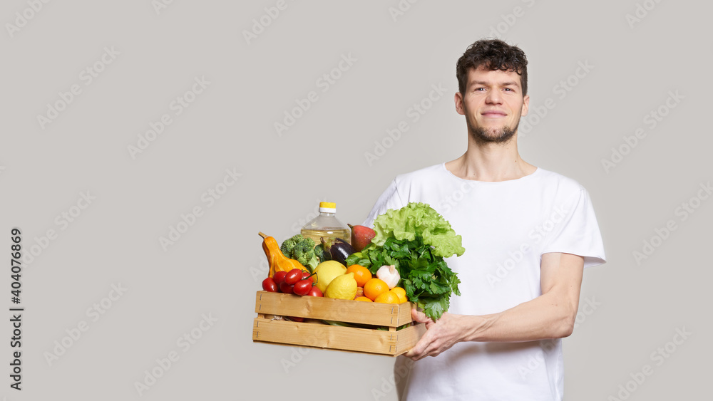 online shopping concept. A man in T-shirt holds a box of fresh food in his hands. Food delivery from the supermarket, from farmers. Delivery during quarantine online shopping concept. A man in T-shirt holds a box of fresh food in his hands. Food delivery from the supermarket, from farmers. Delivery during quarantine