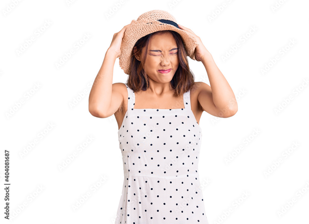 Young beautiful chinese girl wearing summer hat suffering from headache desperate and stressed because pain and migraine. hands on head. Young beautiful chinese girl wearing summer hat suffering from headache desperate and stressed because pain and migraine. hands on head.