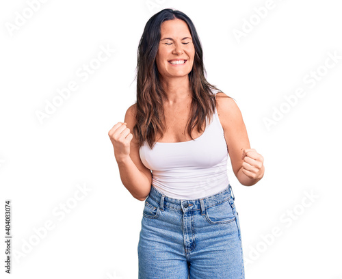 Young beautiful brunette woman wearing casual sleeveless t-shirt very happy and excited doing winner gesture with arms raised  smiling and screaming for success. celebration concept.