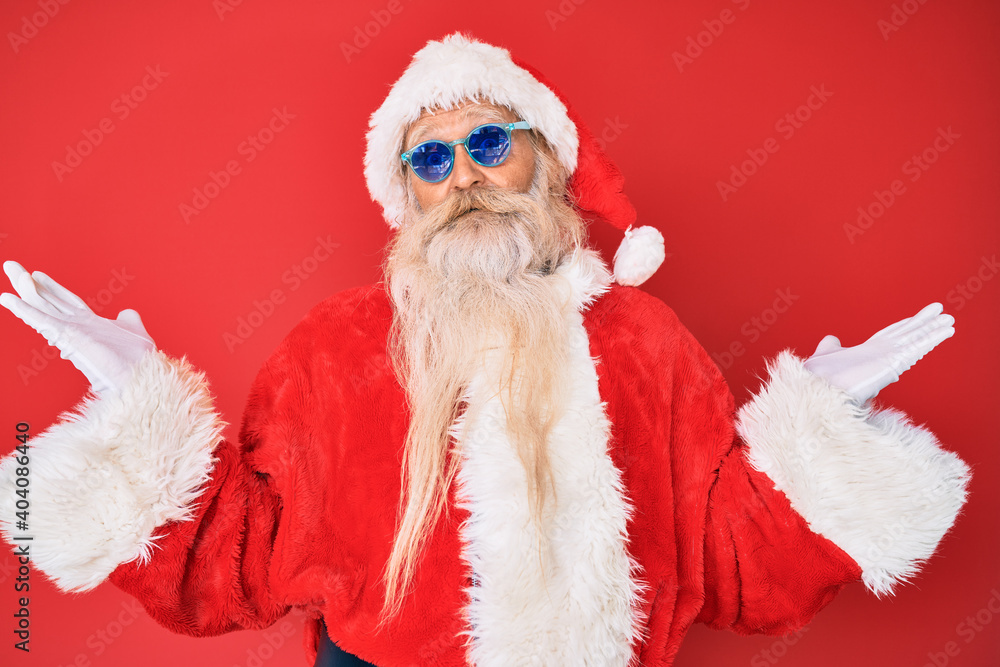 Old senior man wearing santa claus costume and sunglasses celebrating victory with happy smile and winner expression with raised hands