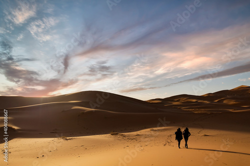  Selective focus  Silhouette of two people walking on the sand dunes of the Merzouga desert during a stunning sunset. Merzouga  Morocco.