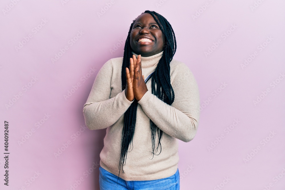 Young black woman with braids wearing casual winter sweater begging and praying with hands together with hope expression on face very emotional and worried. begging. Young black woman with braids wearing casual winter sweater begging and praying with hands together with hope expression on face very emotional and worried. begging.