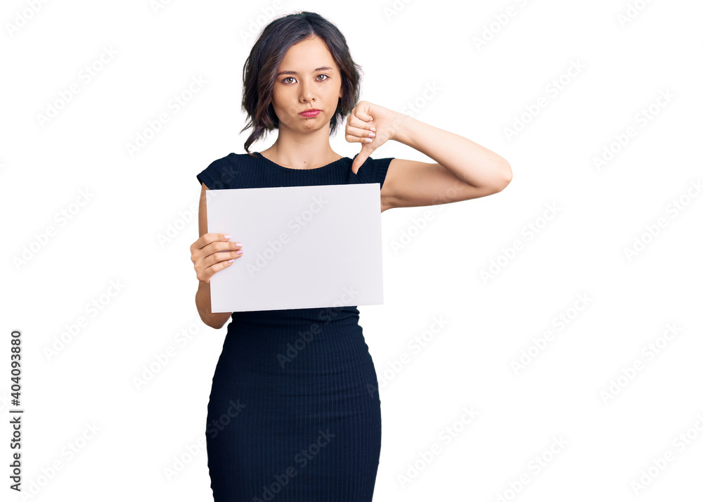 Young beautiful girl holding blank empty banner with angry face, negative sign showing dislike with thumbs down, rejection concept Young beautiful girl holding blank empty banner with angry face, negative sign showing dislike with thumbs down, rejection concept