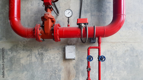Red water or gas pipeline with gate pressure valve and stainless steel test box installed on concrete wall with copy space. Line pipe industrial and extinguisher pump. 