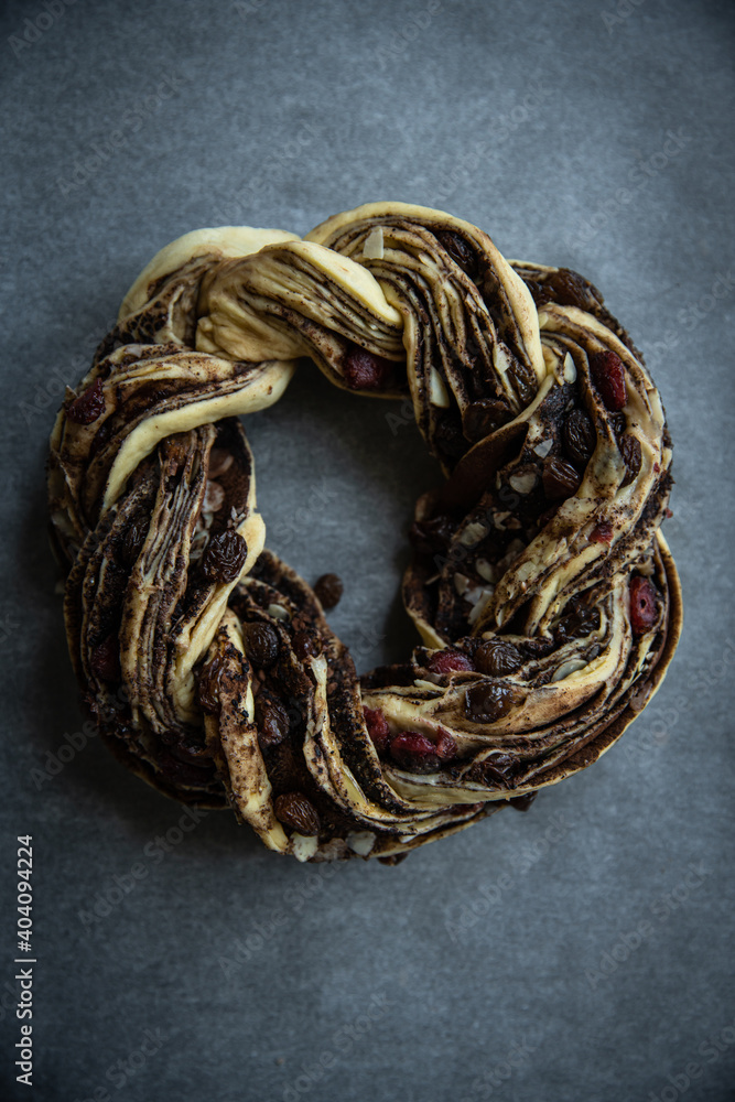 Unbaked homemade yeast dough wreath (Kranz, couronne, brioche ) with chocolate and dried fruits filling on baking sheet on wooden table.