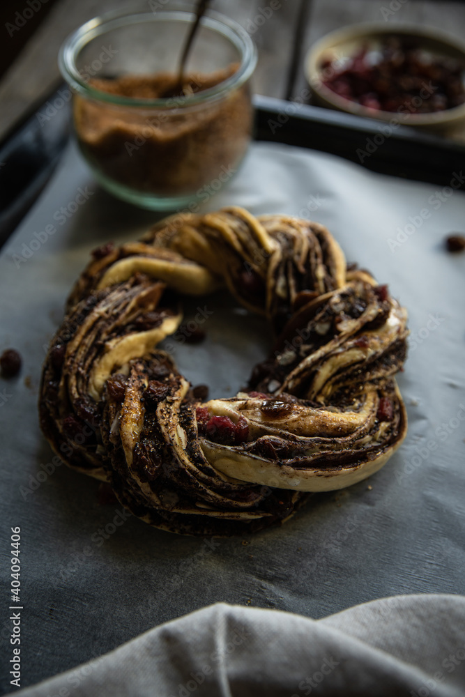 Unbaked homemade yeast dough wreath (Kranz, couronne, brioche ) with chocolate and dried fruits filling and brown sugar on baking sheet on wooden table.