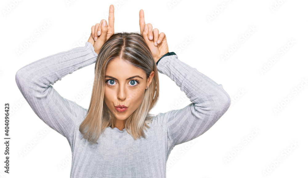 Beautiful blonde woman wearing casual clothes doing funny gesture with finger over head as bull horns