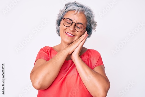 Senior hispanic grey- haired woman wearing casual clothes and glasses sleeping tired dreaming and posing with hands together while smiling with closed eyes.