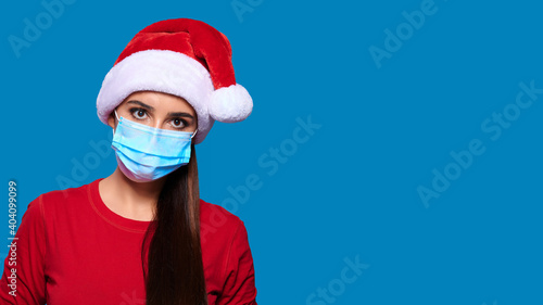 Caucasian woman in protective medical mask and Santa hat on blue isolated background. Christmas on quarantine.