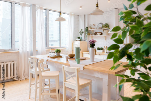 Stylish kitchen in light colors in a trendy modern duplex apartment with large high windows.