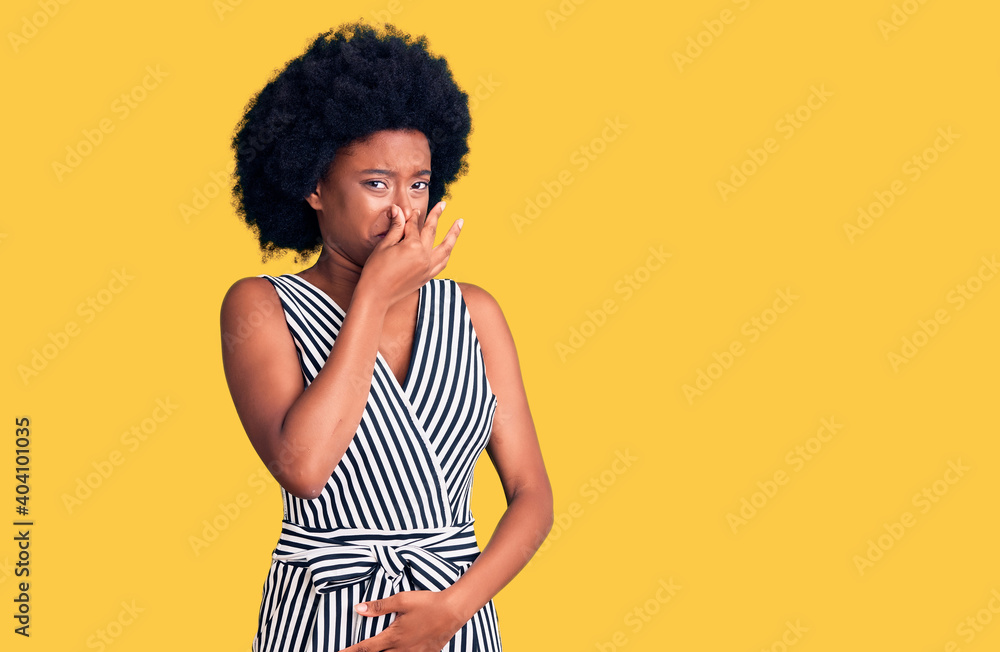 Young african american woman wearing casual clothes smelling something stinky and disgusting, intolerable smell, holding breath with fingers on nose. bad smell Young african american woman wearing casual clothes smelling something stinky and disgusting, intolerable smell, holding breath with fingers on nose. bad smell