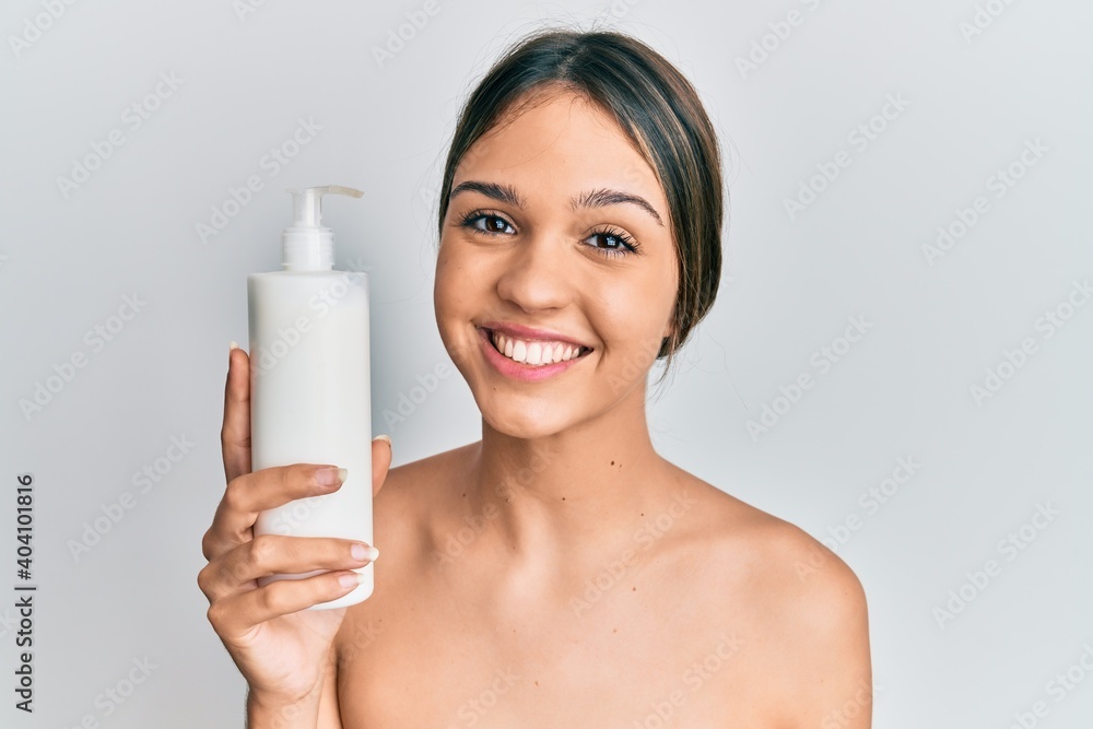 Young brunette woman holding cosmetic moisturizer facial cream looking positive and happy standing and smiling with a confident smile showing teeth Young brunette woman holding cosmetic moisturizer facial cream looking positive and happy standing and smiling with a confident smile showing teeth
