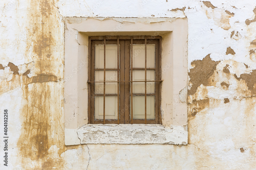 an old wooden window with metallic protection bars on a white wall made of clay