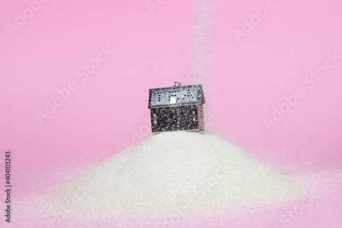 House-shaped tea strainer on a pink background. A strainer for brewing tea on a pile of sugar. Sweet story. House on the hill. Sugar is poured on the house
