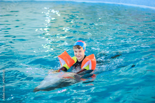 Happy little girl swimming with dolphins in Dolphinarium. Swimming, bathing and communication with dolphins. Treatment of children by means of dolphins. Dolphin therapy. Concept People and dolphins