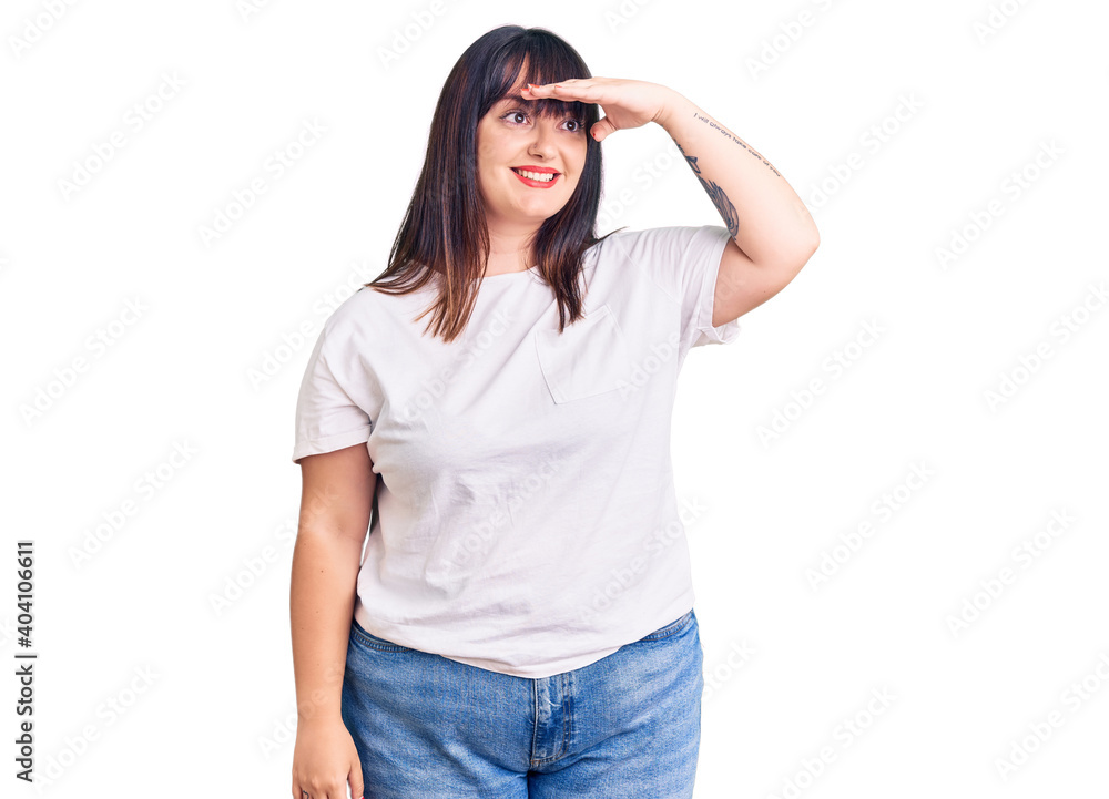 Young plus size woman wearing casual clothes very happy and smiling looking far away with hand over head. searching concept. Young plus size woman wearing casual clothes very happy and smiling looking far away with hand over head. searching concept.