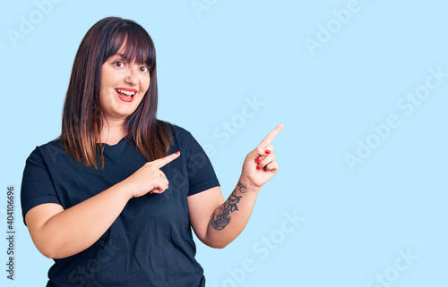 Young plus size woman wearing casual clothes smiling and looking at the camera pointing with two hands and fingers to the side.