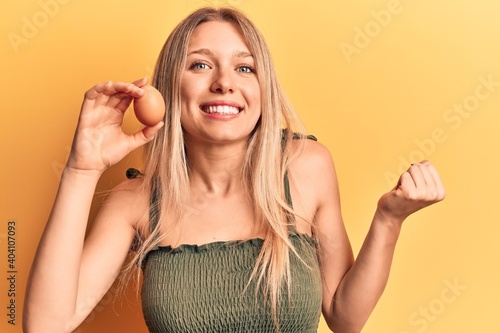 Young blonde woman holding egg screaming proud, celebrating victory and success very excited with raised arm