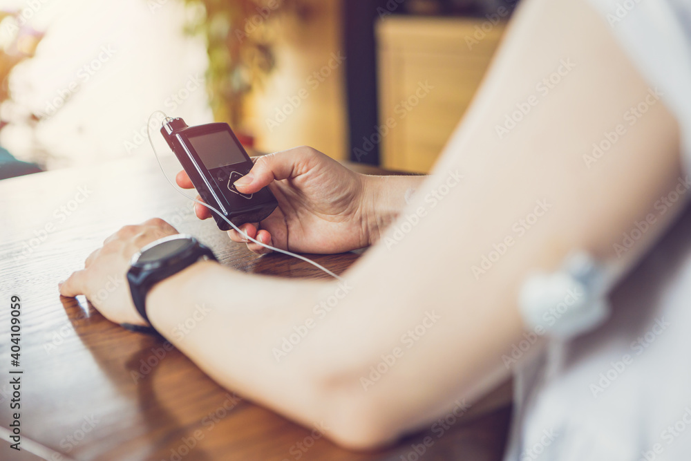 Obraz premium Modern diabetes treatment, woman checking glucose level and dosing insulin using insulin pump and remote sensor on her hand, focus on background