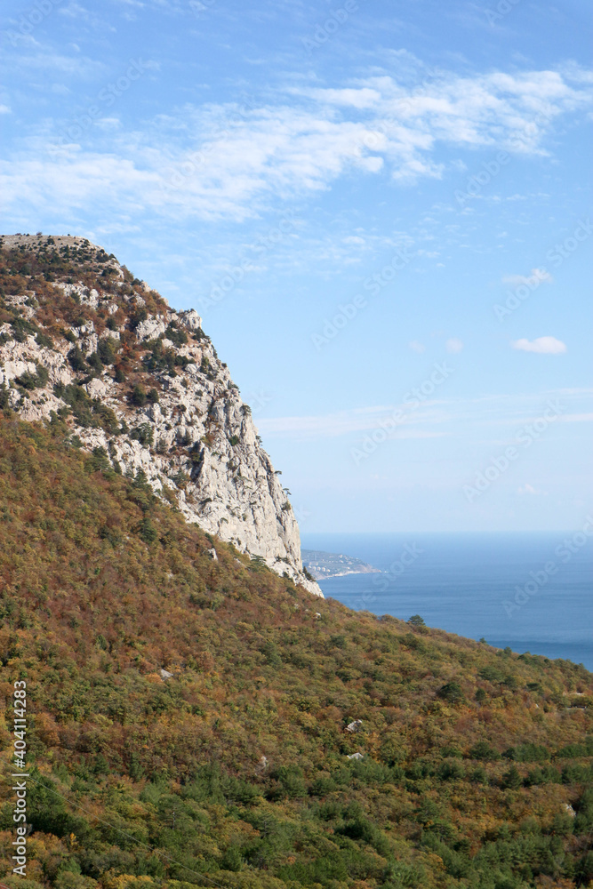 View to the colorful autumn forest on a slope of Crimea mountains with azure black sea on the background