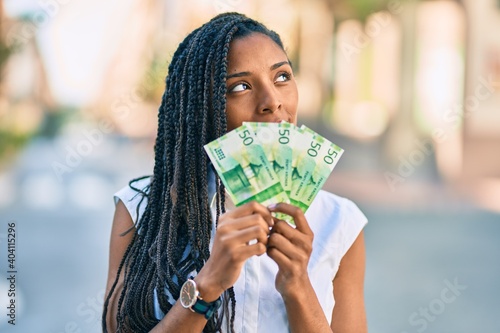 Young african american woman covering mouth with norwegian 50 krona banknotes at the city.