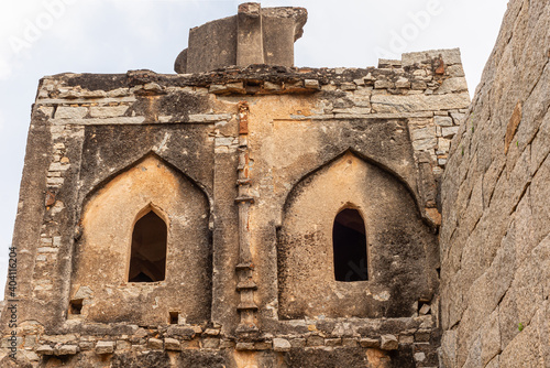 Hampi, Karnataka, India - November 5, 2013: Zanana Enclosure. Closeup of Brown stone ruinous damaged upper level of watchtower along external wall under silver sky. photo